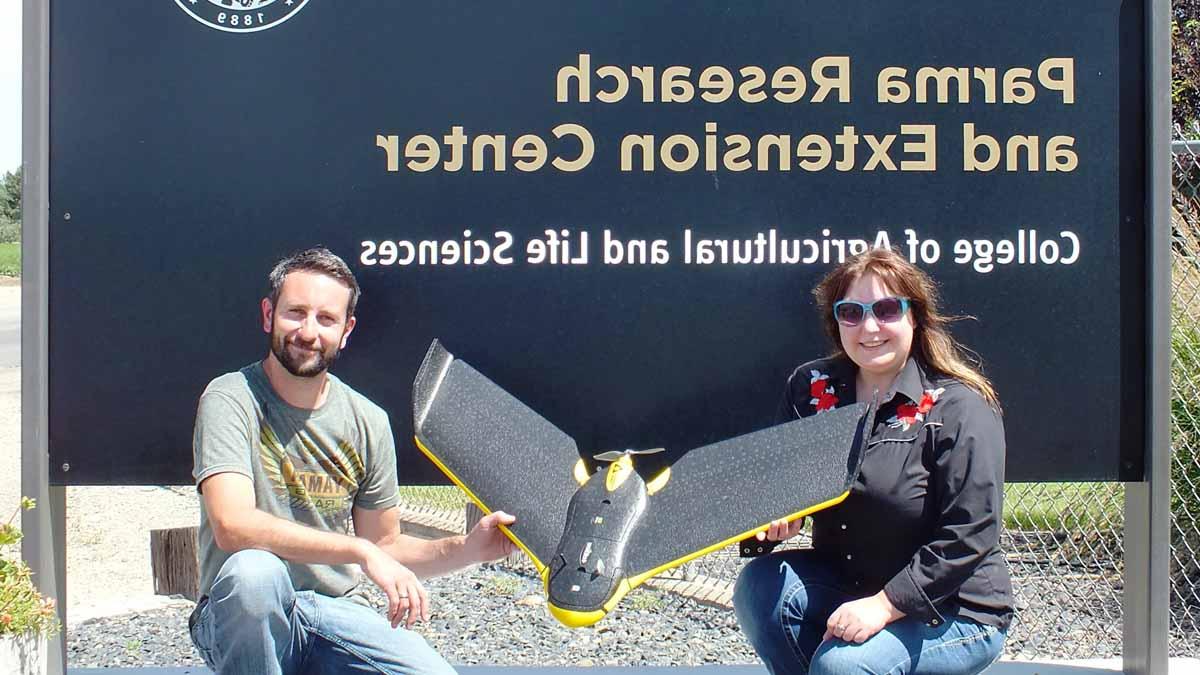 Two people holding a drone in front of the Parma Research and Extension Center sign