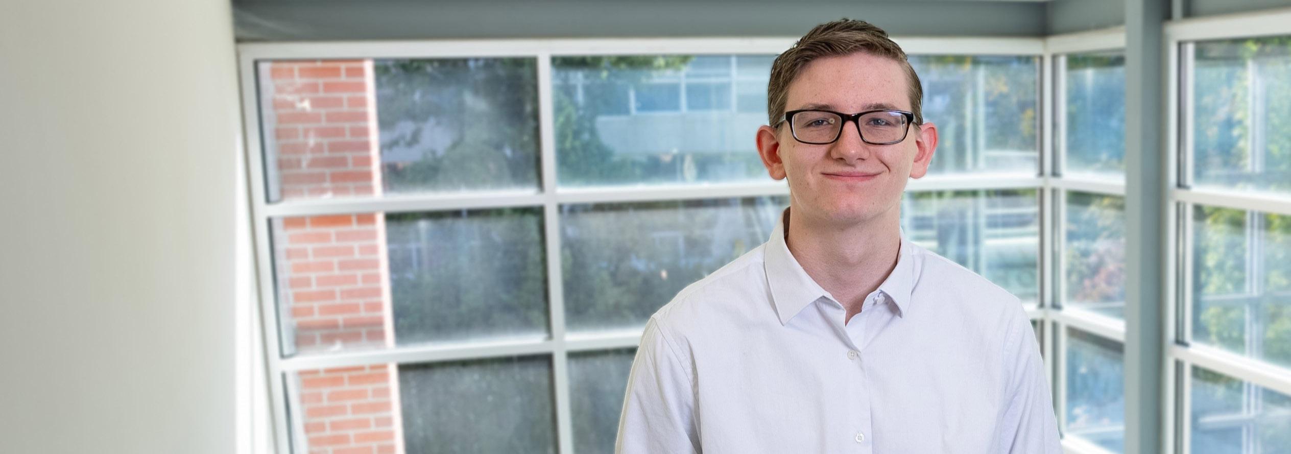 Young man with glasses st和s in front of window.