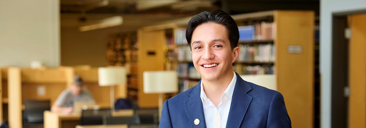 Student standing in a library looking at the camera smiling.